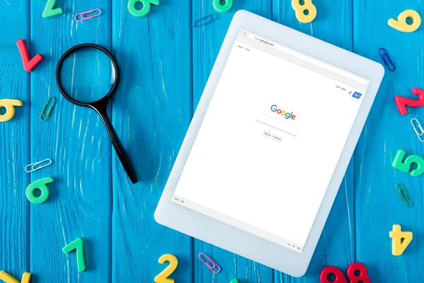Vue du dessus de la tablette numérique avec google site Web à l'écran, loupe, trombones et numéros colorés sur fond bleu en bois — Photo de stock