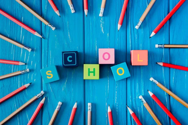 Draufsicht auf den Schriftzug Schule aus Würfeln, umgeben von Bleistiften auf blauem Holzgrund — Stockfoto