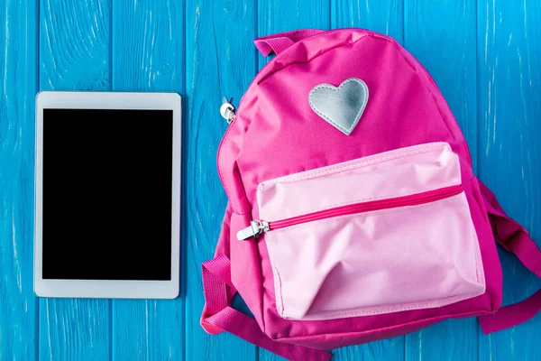 Ansicht des digitalen Tablets mit leerem Bildschirm und rosa Rucksack auf blauem Holzhintergrund — Stockfoto