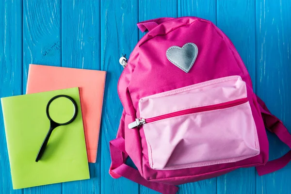 Верхний вид учебников, лупа и розовый рюкзак на синем деревянном фоне — стоковое фото