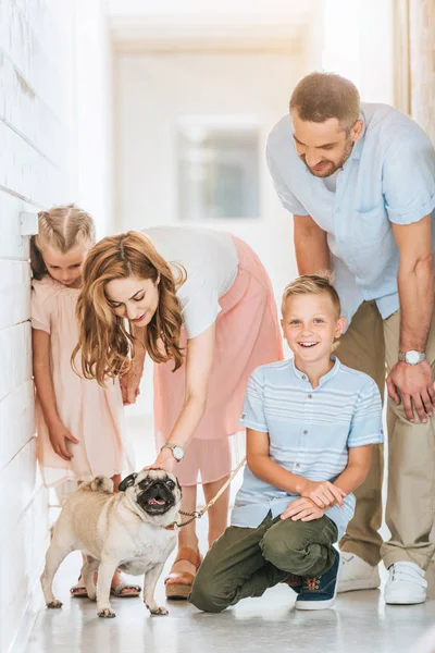 Pais e crianças palming adotivo cão pug no abrigo animais — Fotografia de Stock