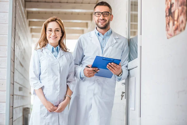 Two veterinarians in white coats standing in veterinary clinic and looking at camera — Stock Photo