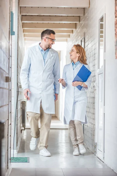 Vétérinaires en manteaux blancs marchant avec des presse-papiers dans une clinique vétérinaire et se regardant — Photo de stock