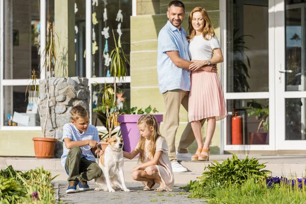 Happy parents looking at children playing with dog outside house — Stock Photo