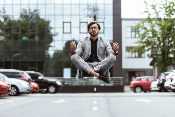 Handsome young businessman floating in air in lotus pose and meditating at parking — Stock Photo