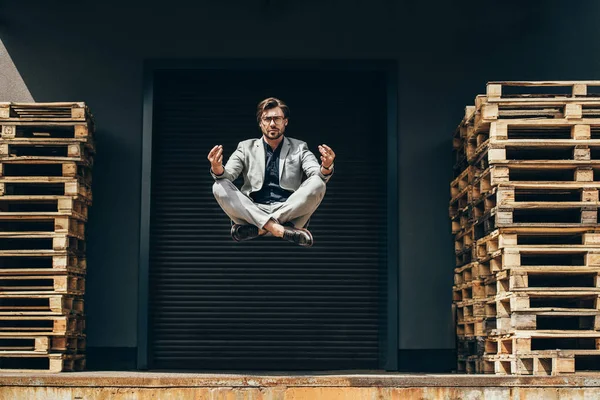 Bonito jovem empresário flutuando no ar em pose de lótus e meditando na frente do portão do rolo — Fotografia de Stock