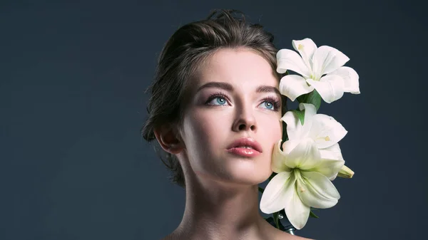 Крупный план портрета привлекательной молодой женщины с белыми лилиями, смотрящей в сторону изолированной на сером — стоковое фото