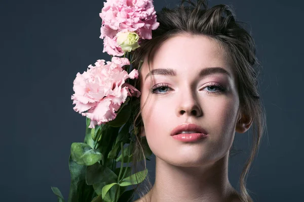 Close-up retrato de bela jovem com flores eustoma rosa atrás da orelha olhando para a câmera isolada no cinza — Fotografia de Stock