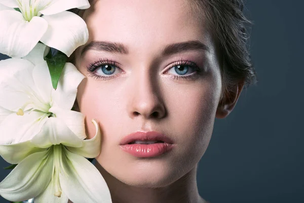 Retrato de cerca de una atractiva joven rodeada de flores de lilium blanco aisladas en gris - foto de stock