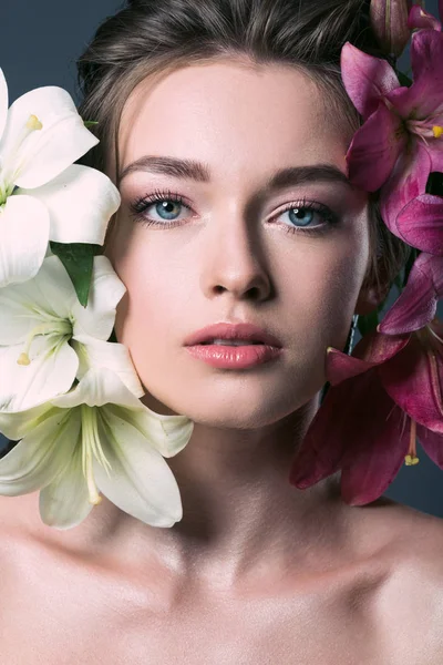 Nahaufnahme Porträt einer schönen jungen Frau, umgeben von liliumfarbenen Blumen auf grau — Stockfoto