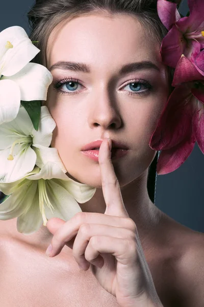 Nahaufnahme Porträt einer schönen jungen Frau, umgeben von liliumfarbenen Blumen, die eine Geste der Stille zeigen — Stockfoto