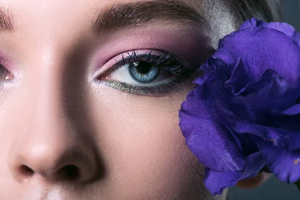 Retrato parcial de una hermosa joven con sombras de ojos rosados y flor de eustoma púrpura - foto de stock