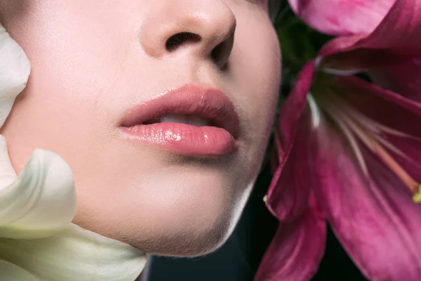 Partial portrait of beautiful young woman with pink lips and lilium flowers on grey — Stock Photo