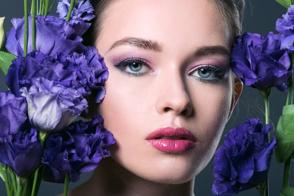 Close-up portrait of attractive young woman with eustoma flowers around looking at camera isolated on grey — Stock Photo