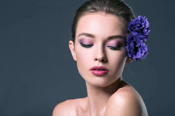 Belle jeune femme avec des fleurs d'eustomie dans les cheveux et les yeux fermés isolés sur gris — Photo de stock