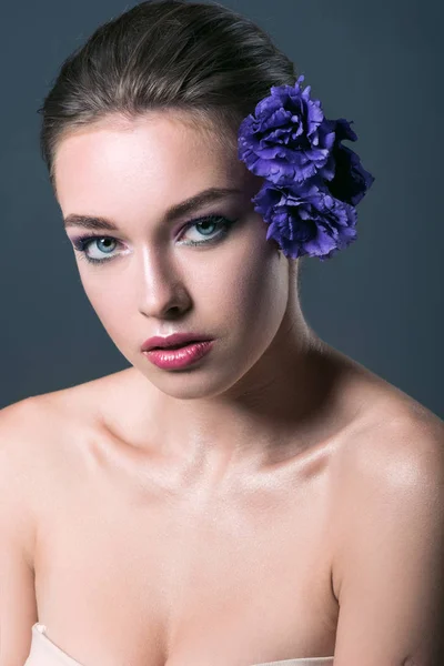 Приваблива молода жінка з квітами еустоми в волоссі дивиться на камеру ізольовано на сірому — стокове фото