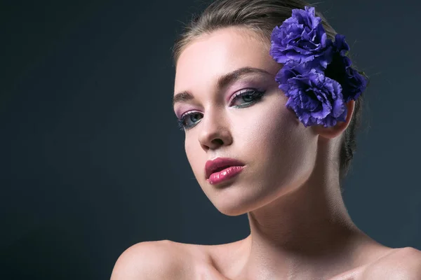 Retrato de cerca de una joven seductora con flores de eustoma detrás de la oreja mirando a la cámara aislada en gris - foto de stock