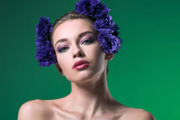 Close-up portrait of attractive young woman with eustoma flowers on head looking at camera isolated on green — Stock Photo