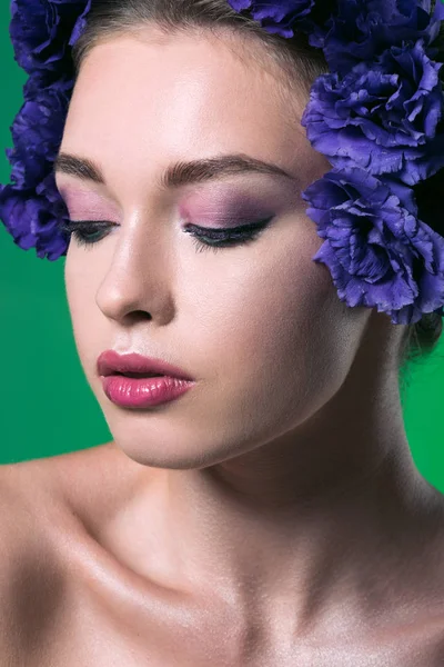 Retrato de cerca de la hermosa mujer joven con flores de eustoma en la cabeza y los ojos cerrados aislados en verde - foto de stock