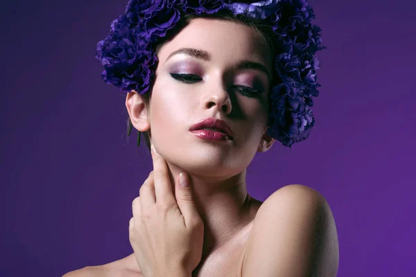 Close-up portrait of tender young woman with eustoma flowers wreath on head looking at camera isolated on purple — Stock Photo