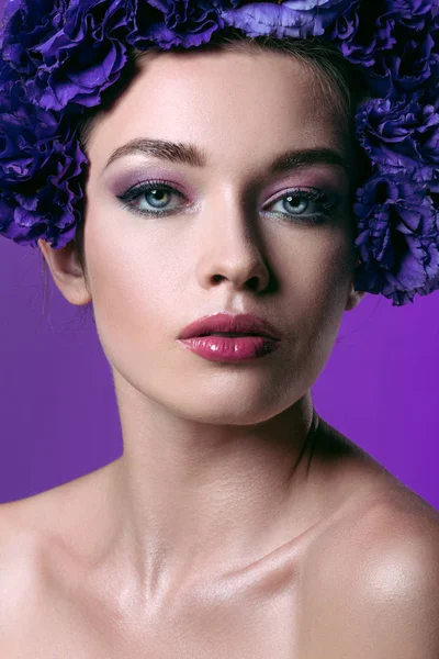 Close-up portrait of beautiful young woman with eustoma flowers wreath on head looking at camera isolated on purple — Stock Photo