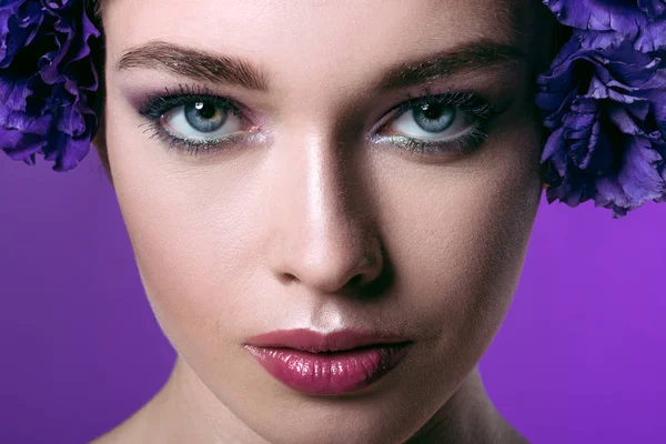 Close-up portrait of attractive young woman with eustoma flowers wreath on head looking at camera isolated on purple — Stock Photo