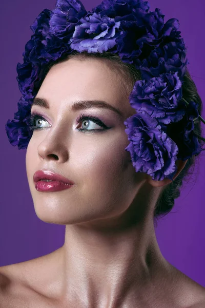 Крупным планом портрет красивой молодой женщины с венком из цветов эустомы на голове, смотрящей в сторону, изолированной на фиолетовый — стоковое фото