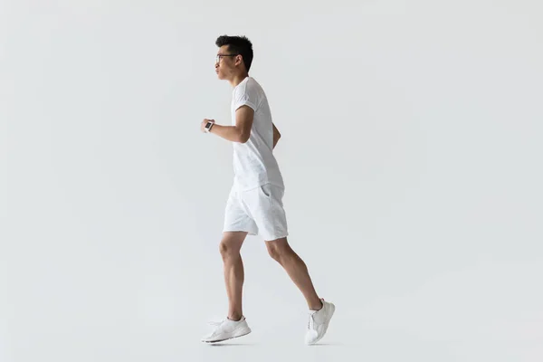 Side view of young asian sportsman running on grey background — Stock Photo