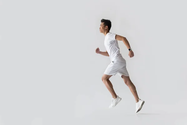 Vista lateral de joven asiático atleta corriendo sobre fondo gris - foto de stock