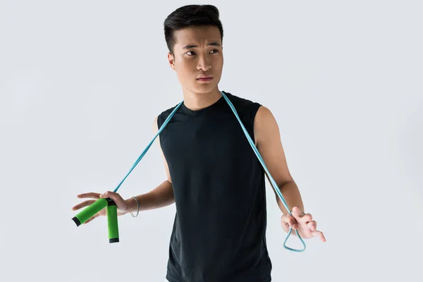 Serious young asian sportsman standing jump rope isolated on grey background — Stock Photo