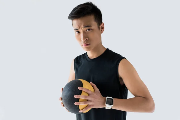 Serious asian sportsman with smartwatch holding medicine ball isolated on grey background — Stock Photo