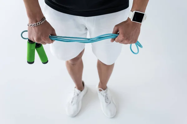 Imagem recortada de jovem atleta do sexo masculino com smartwatch segurando corda de salto no fundo cinza — Fotografia de Stock