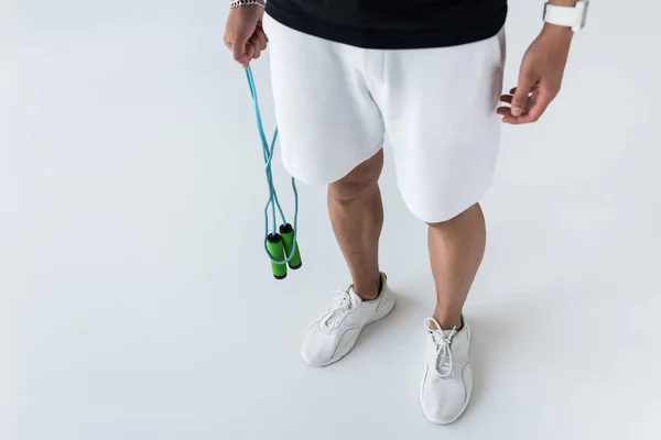 Cropped image of young sportsman with smartwatch holding jump rope on grey background — Stock Photo