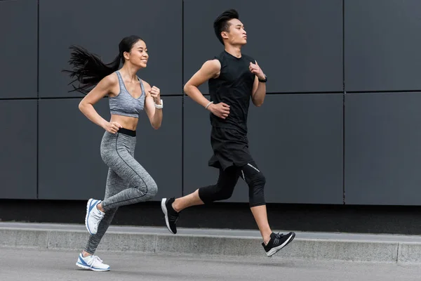 Side view of asian sportsman and sportswoman running at city street — Stock Photo