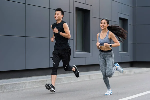 Smiling asian female and male athletes running at urban street — Stock Photo