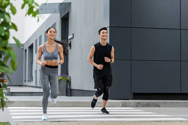 Smiling asian sportsman and sportswoman running at city street — Stock Photo
