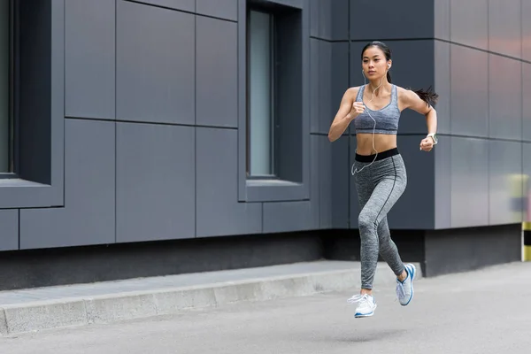 Atractivo joven asiático sportswoman en auriculares corriendo en ciudad calle — Stock Photo