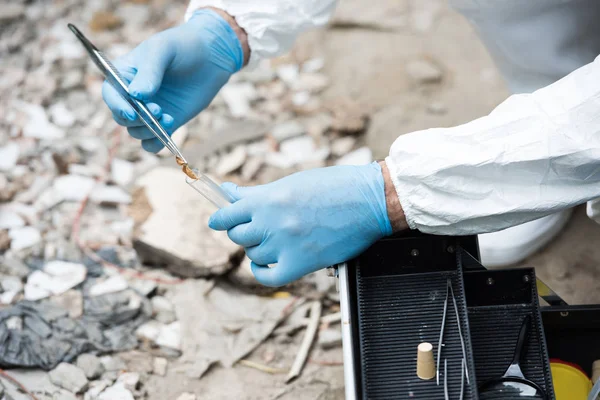 Imagen recortada de científico masculino en guantes de látex poniendo hoja seca por pinzas en frasco de prueba al aire libre — Stock Photo