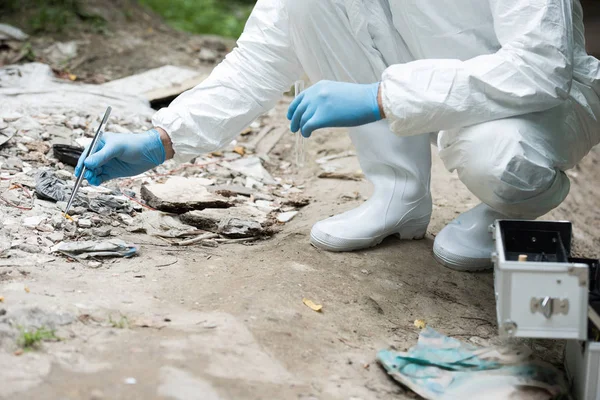 Imagen recortada de científico masculino en guantes de látex tomando muestra de piedra por pinzas al aire libre - foto de stock