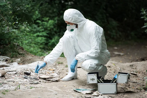 Vista lateral del científico masculino en guantes de látex tomando muestra de piedra por pinzas al aire libre - foto de stock