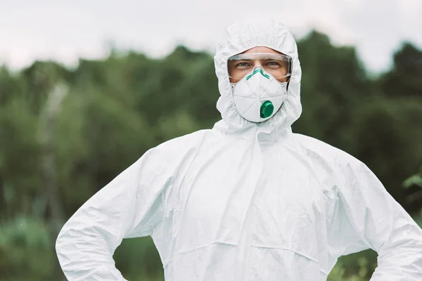 Enfoque selectivo de sonriente científico masculino en máscara protectora y traje mirando a la cámara al aire libre - foto de stock