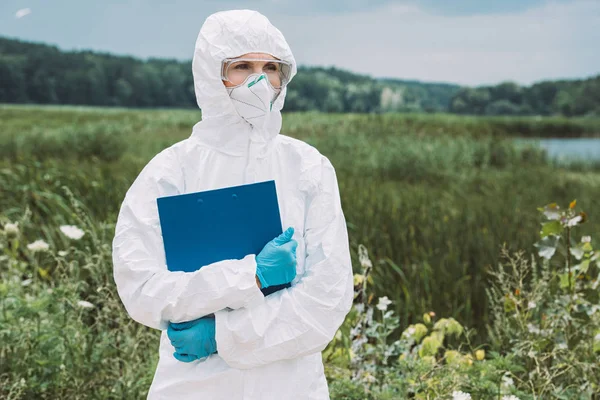 Foyer sélectif du scientifique femelle en combinaison de protection et googles tenant presse-papiers dans la prairie — Photo de stock