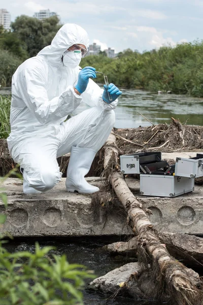 Wissenschaftler in Schutzanzug und Maske legen Bodenprobe mit Pinzette in Testkolben im Freien — Stockfoto