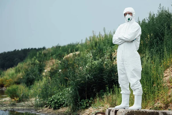 Mâle scientifique en combinaison de protection et masque debout près de l'eau à l'extérieur — Photo de stock