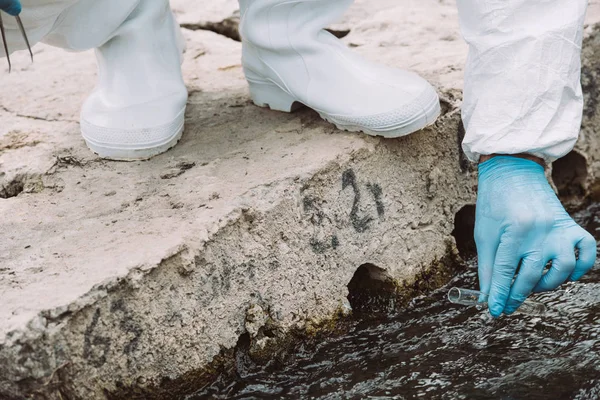 Abgeschnittenes Bild eines männlichen Wissenschaftlers in Latexhandschuhen, der im Freien eine Wasserprobe in einem Testkolben entnimmt — Stockfoto