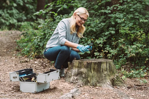 Femme scientifique en gants de latex regardant rameau par loupe dans la forêt — Photo de stock