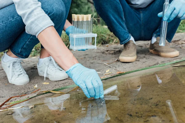 Male and female scientists taking sample of water in test flask outdoors — Stock Photo