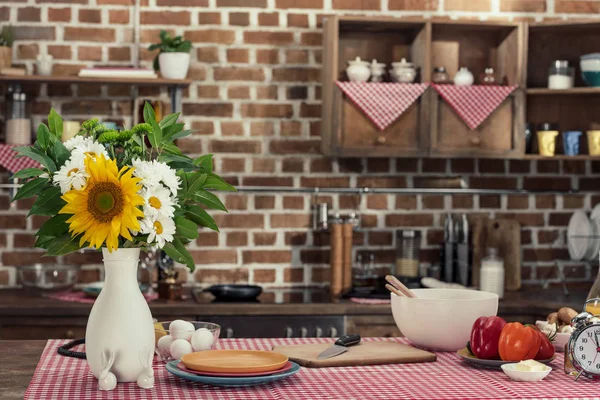 Mesa de cocina con ramo de flores y varios productos en la cocina estilo loft - foto de stock