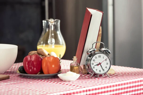 Reloj despertador vintage con varios productos y libro de recetas en la mesa - foto de stock