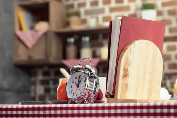 Recipes book with alarm clock on cooking table at kitchen — Stock Photo